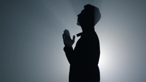 Silueta náboženský muž šeptající modlitby uvnitř. Věřící se modlí ve tmě. - Záběry, video