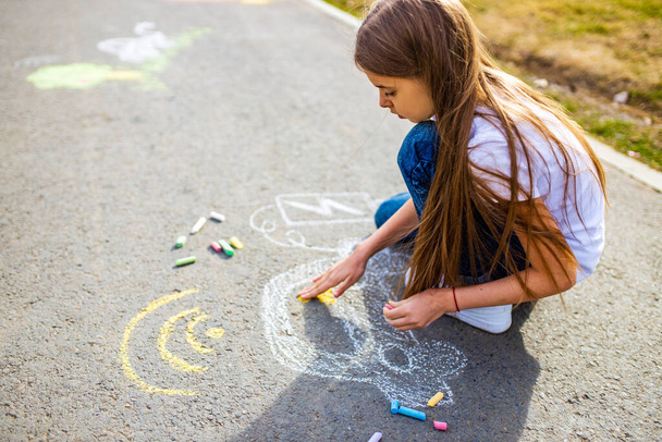 Little girl with creative craft hobby drawing electro on the asphalt with chalk car environment, eco friendly, save energy in park at summer day - Фото, зображення