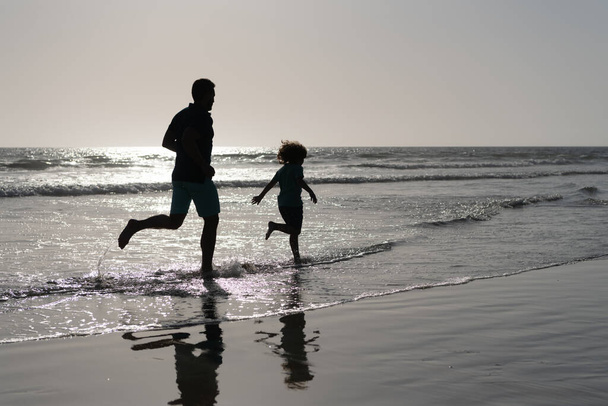 父と息子のシルエットが夏のビーチで楽しく自由を感じながら走り夏休み - 写真・画像