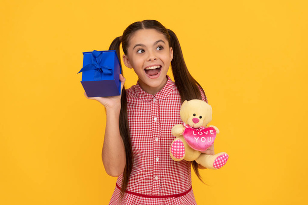 amazed child hold bear toy and gift box on yellow background, womens day - Photo, Image