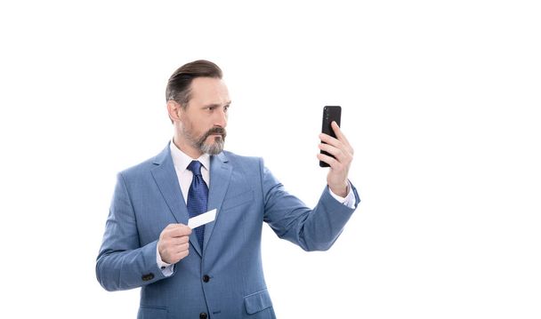 serio maduro jefe en traje celebrar tarjeta de crédito y teléfono aislado en blanco, selfie - Foto, imagen