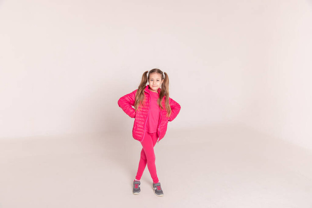 una ragazza con le code su uno sfondo bianco. bambino in giacca rosa. Copia spazio - Foto, immagini