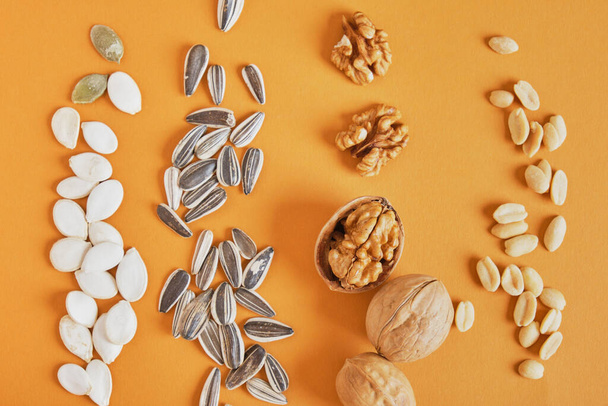 a handful of different nuts and seeds on a brown background, peanuts, sunflower seeds, pumpkin and walnut - Foto, Imagem