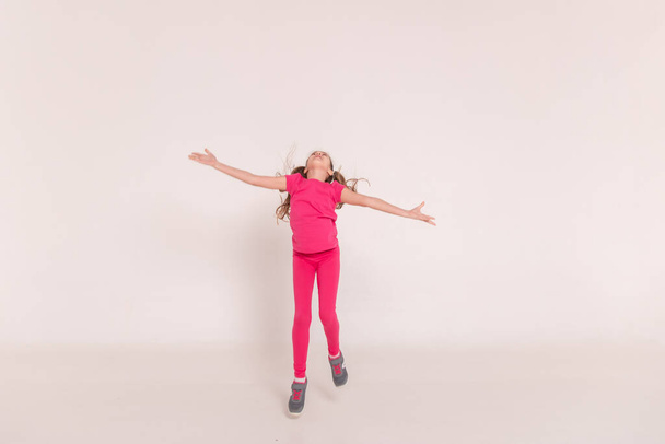a beautiful girl in a pink jumps and smiles on a white background. happy childhood. Copy space - Φωτογραφία, εικόνα