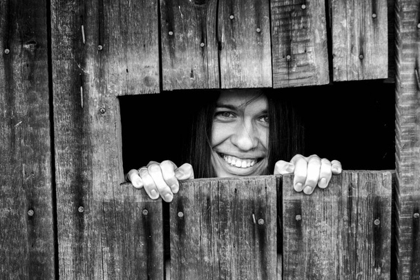 Egy fiatal nő kukucskál be egy kis ablakon. Fekete-fehér fénykép. - Fotó, kép