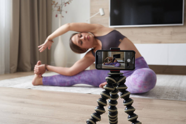 Genç bayan blogcu oturma odasında yoga yaparken spor videosu kaydediyor. - Fotoğraf, Görsel