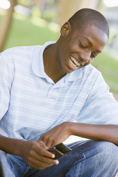 Teenage Boy Sitting Outdoors Using Mobile Phone - Photo, image