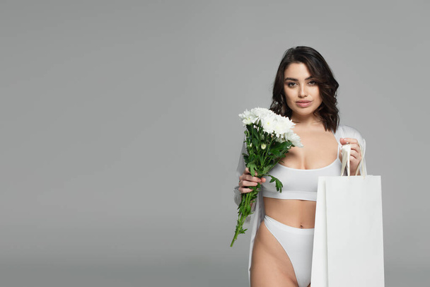 Gorgeous woman in underwear holding bouquet and shopping bag isolated on grey - Photo, Image