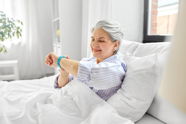 happy old woman with health tracker sitting in bed - 写真・画像