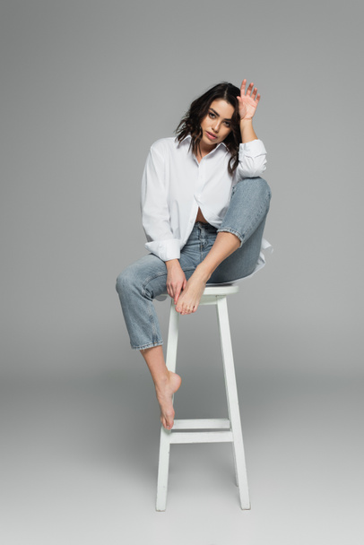Young brunette woman sitting on chair on grey background  - Foto, afbeelding