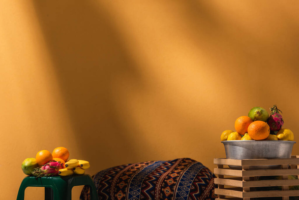 frutas exóticas en el taburete y en un tazón de metal sobre fondo naranja sobre naranja - Foto, Imagen