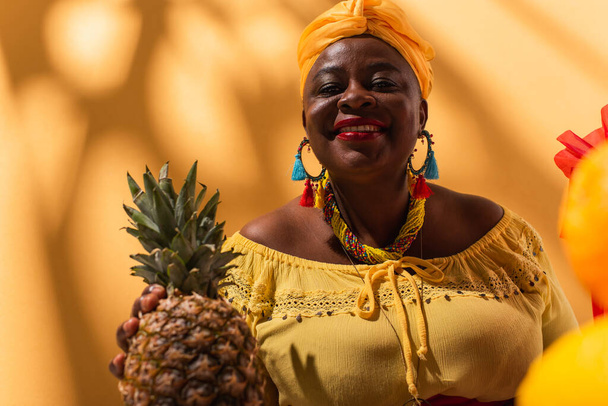 smiling middle aged african american woman holding pineapple in hand on orange - Fotoğraf, Görsel