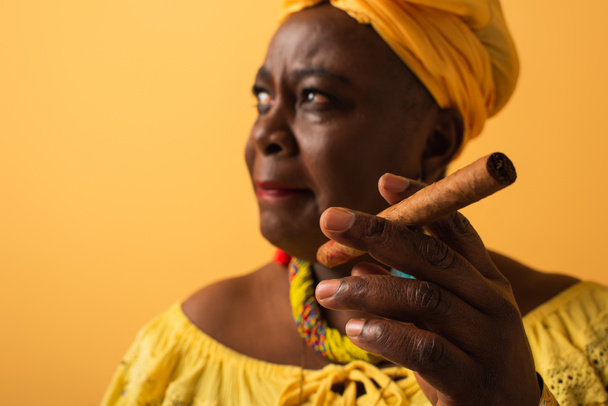 middle aged african american woman in yellow turban and blouse holding cigar on yellow - Fotografie, Obrázek