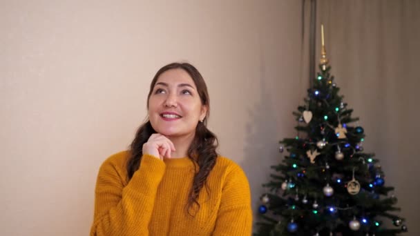 Mujer joven pide un deseo en voz alta sobre el fondo de un árbol de Navidad decorado - Metraje, vídeo