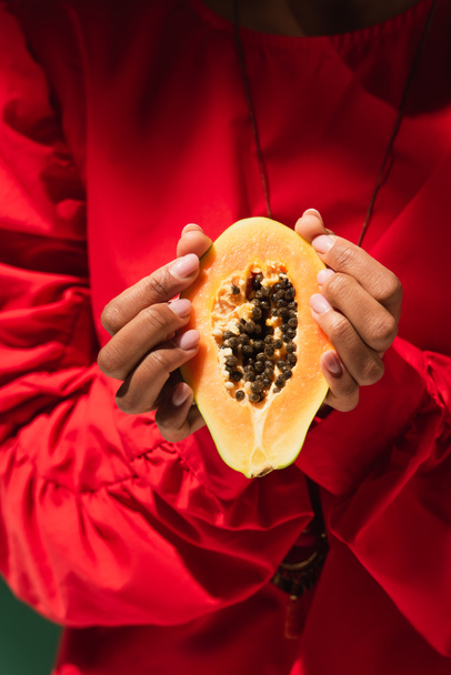 Nahaufnahme des halben Papayaschnitts in den Händen einer jungen afrikanisch-amerikanischen Frau in roter Bluse - Foto, Bild