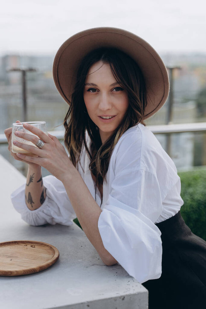 fashion photo of a cheeky woman dressed in a stylish white dress with a black designer belt posing with drink outdoor on a bright terrace - Foto, Bild