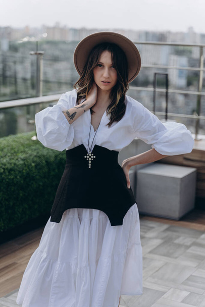fashion photo of a cheeky woman dressed in a stylish white dress with a black designer belt posing outdoor on a bright terrace - Foto, Imagen