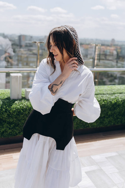 fashion photo of a glamorous woman dressed in a stylish white dress with a black designer belt posing outdoor on a bright terrace - Zdjęcie, obraz