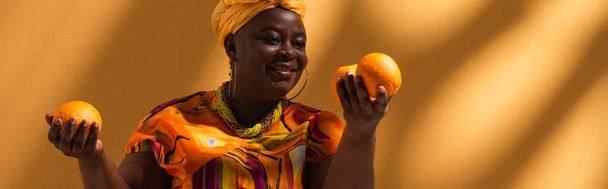 smiling middle aged african american woman holding oranges on background with shadows, banner - Fotoğraf, Görsel
