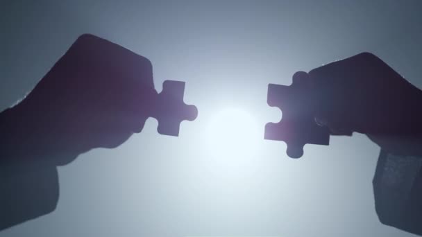 Silhouette hands connecting parts puzzle indoors. Arms matching pieces jigsaw. - Footage, Video
