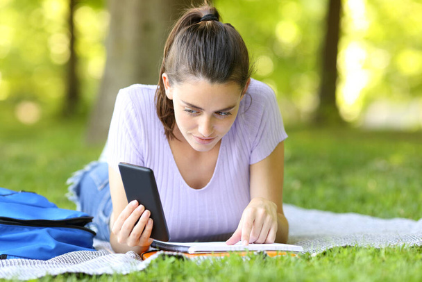 Student learning comparing notes with smart phone content in a campus - Foto, imagen