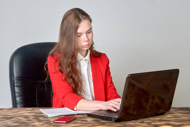 Nainen istuu pöydän ääressä ja käyttää kannettavaa tietokonetta ja lehtiötä. - Valokuva, kuva