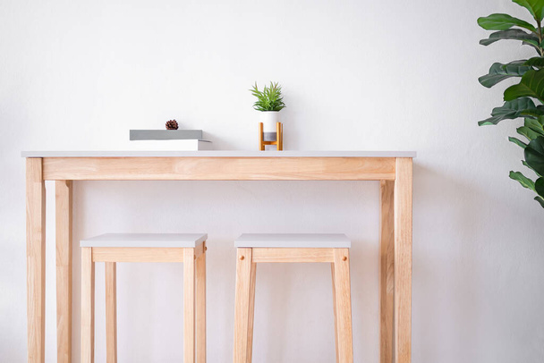 Arbre artificiel réaliste dans un vase sur une table en bois avec chaise et mur en ciment blanc. luxe moderne salon intérieur concept de maison. - Photo, image