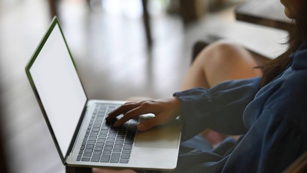 Una bella donna sta scrivendo al computer mentre era seduta sulla poltrona di legno. - Foto, immagini