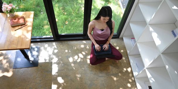 Kobieta używa laptopa, który kładzie się na kolanach w wygodnym salonie.. - Zdjęcie, obraz