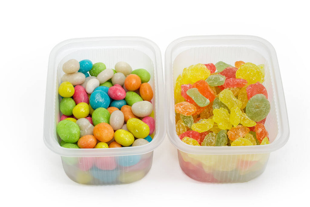 Gekleurde suikersnoepjes en snoepjes gemaakt van de geglazuurde rozijnen in twee kleine plastic containers, close-up op een witte achtergrond - Foto, afbeelding