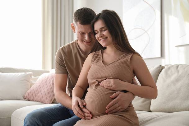 Man touching his pregnant wife's belly at home - Photo, image