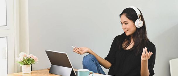 A beautiful woman is using a computer tablet and making a video conference at the wooden working desk. - Photo, Image