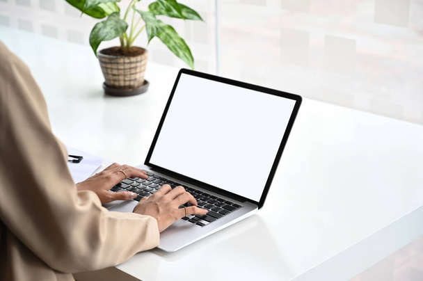 Oříznutý obrázek ženy používá počítač notebook s bílou prázdnou obrazovkou na bílém pracovním stole. - Fotografie, Obrázek