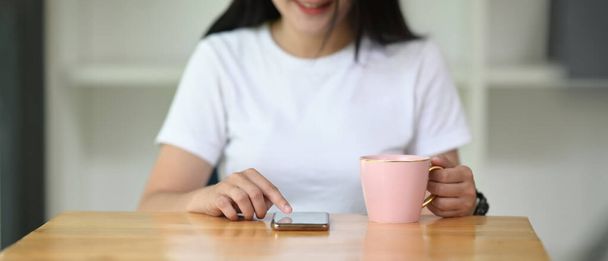 Обрізана жінка використовує смартфон, тримаючи чашку кави в руці
. - Фото, зображення