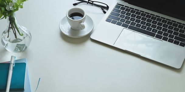 kávécsésze, laptop és egyéb irodai berendezések fehér munkaasztalon  - Fotó, kép