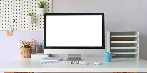 ordenador de pantalla blanca con taza de café, estantería, ratón inalámbrico, teclado, portátil, portalápices, flores en la cesta de mimbre y libros - Foto, Imagen