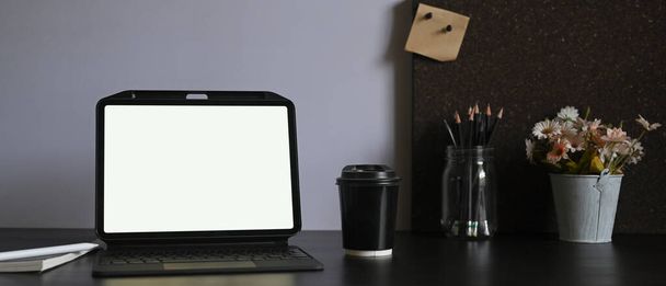 Ein weißes Tablet mit leerem Bildschirm steht auf einem Arbeitstisch, umgeben von verschiedenen Geräten.. - Foto, Bild