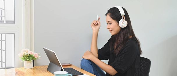 Piękna kobieta używa tabletu komputerowego i robi wideokonferencję przy drewnianym biurku.. - Zdjęcie, obraz