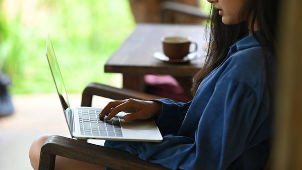 Close-up kobieta jest za pomocą laptopa komputerowego podczas siedzenia na drewnianym krześle. - Zdjęcie, obraz
