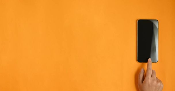 hand using blank screen smartphone on orange background. - Foto, afbeelding