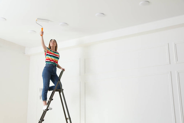 Young woman painting ceiling with white dye indoors, space for text - Foto, imagen