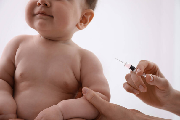 Doctor vaccinating baby against light background, closeup. Health care - Photo, image