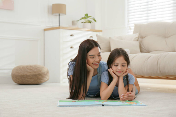 Young mother and her daughter reading book at home, space for text - Фото, изображение