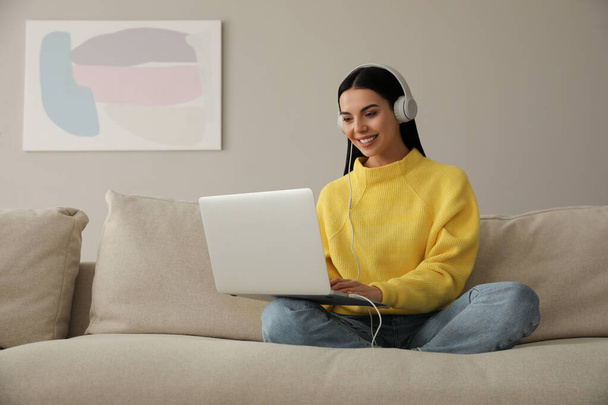Femme avec ordinateur portable et écouteurs assis sur le canapé à la maison - Photo, image
