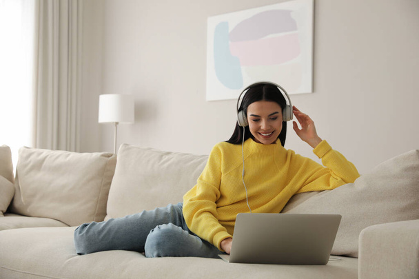 Woman with laptop and headphones sitting on sofa at home - Photo, image