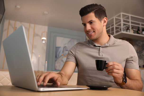 Man with cup of coffee working on laptop at cafe in morning - Фото, изображение