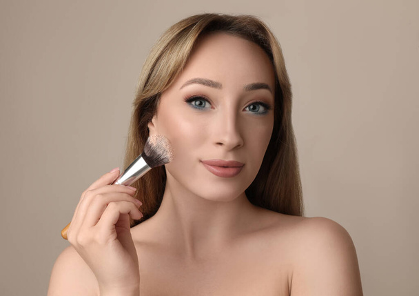 Beautiful young woman applying face powder with brush on grey background - Foto, immagini