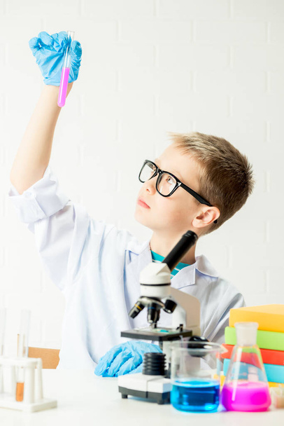 A schoolboy with a microscope examines chemicals in test tubes, conducts experiments - a portrait on a white background. Concept for the study of coronavirus in the laboratory - Foto, Imagem