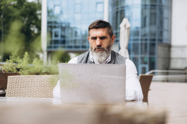 Älterer Mann mit grauem Bart verbringt Zeit im Freien im Laptop. - Foto, Bild