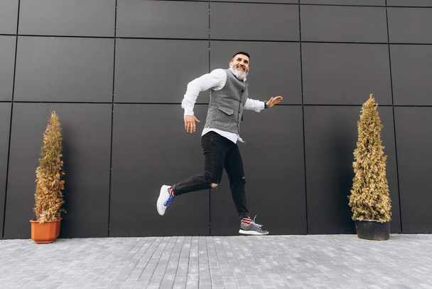 Позитивный жестокий бородатый седовласый мужчина прыгает по чистым городским местам - Фото, изображение